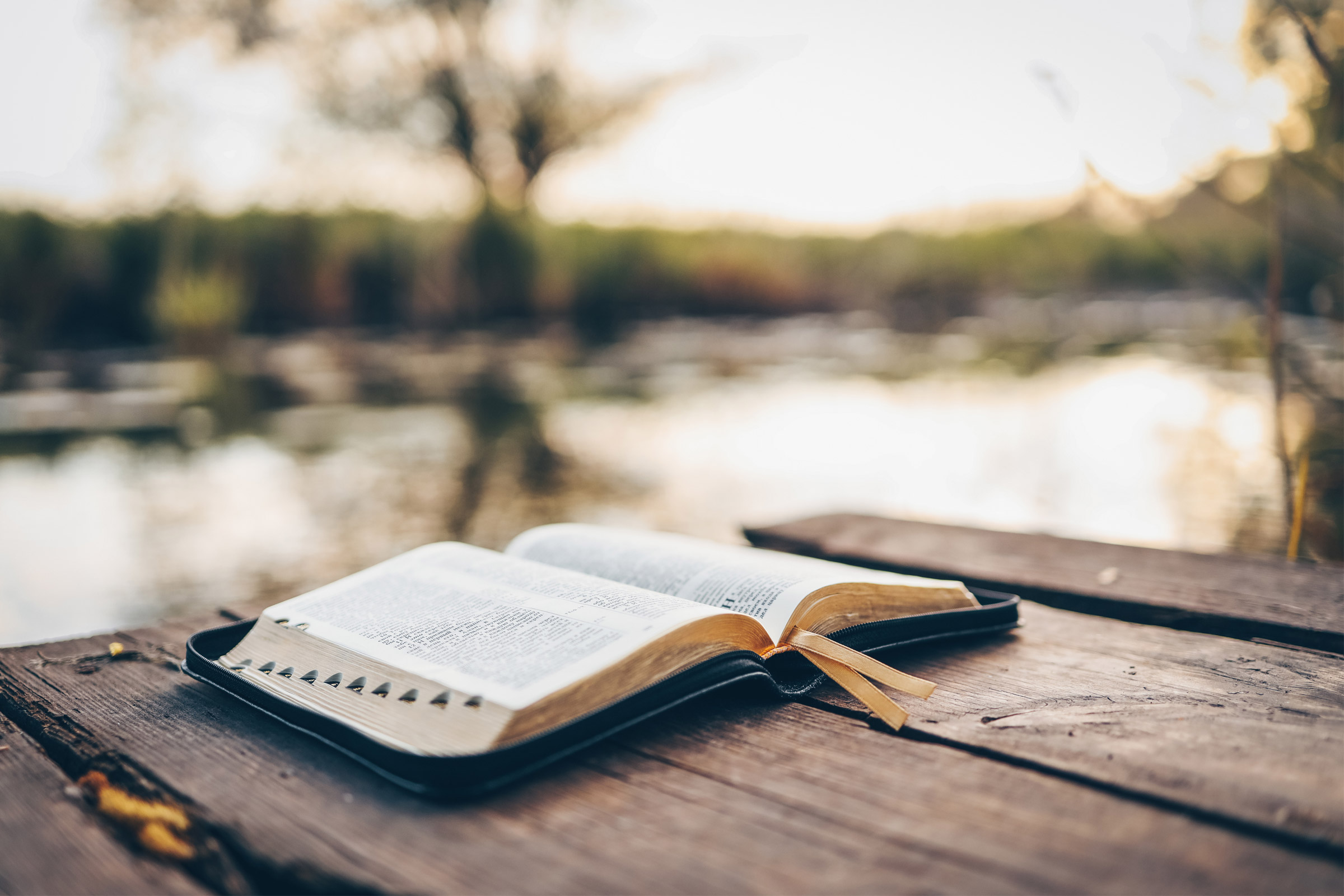 Open book on wooden table by lake