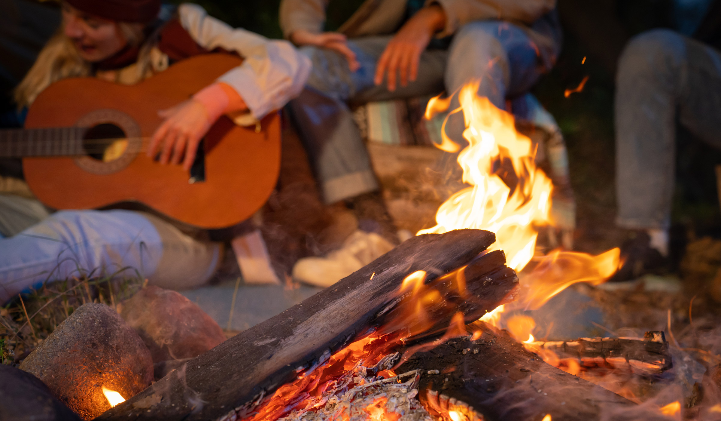 Campfire with people playing guitar nearby