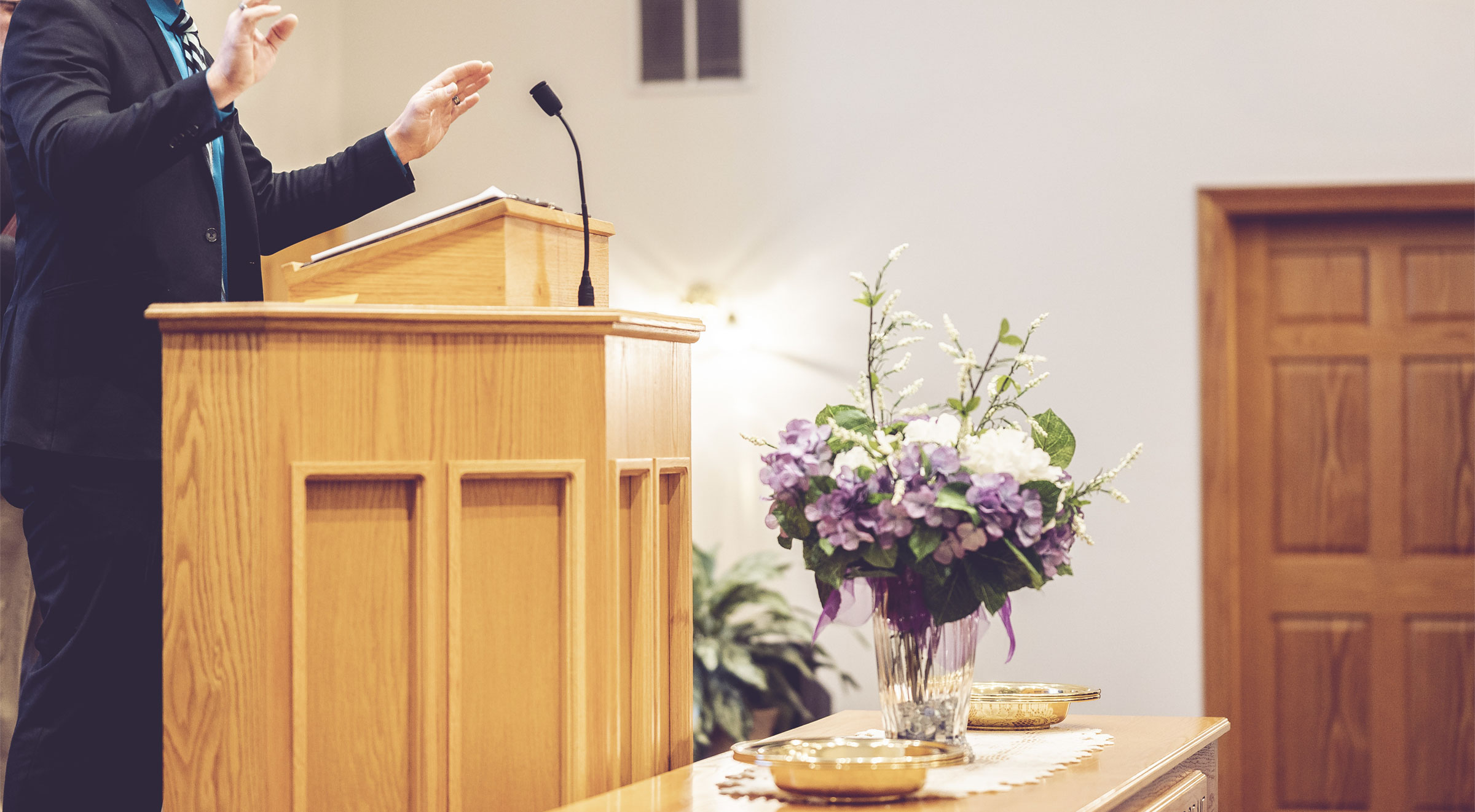 Person speaking at a church podium with flowers.