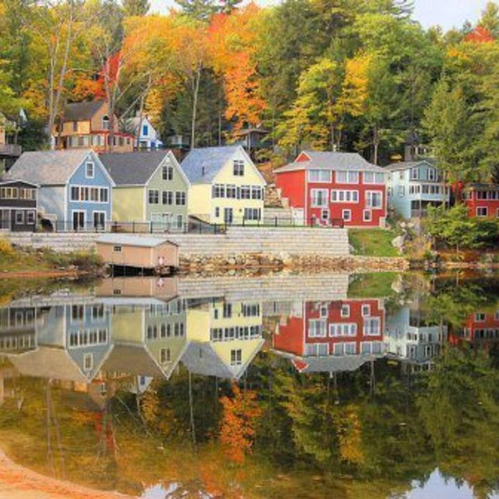 Colorful houses reflected in calm lake with autumn trees.