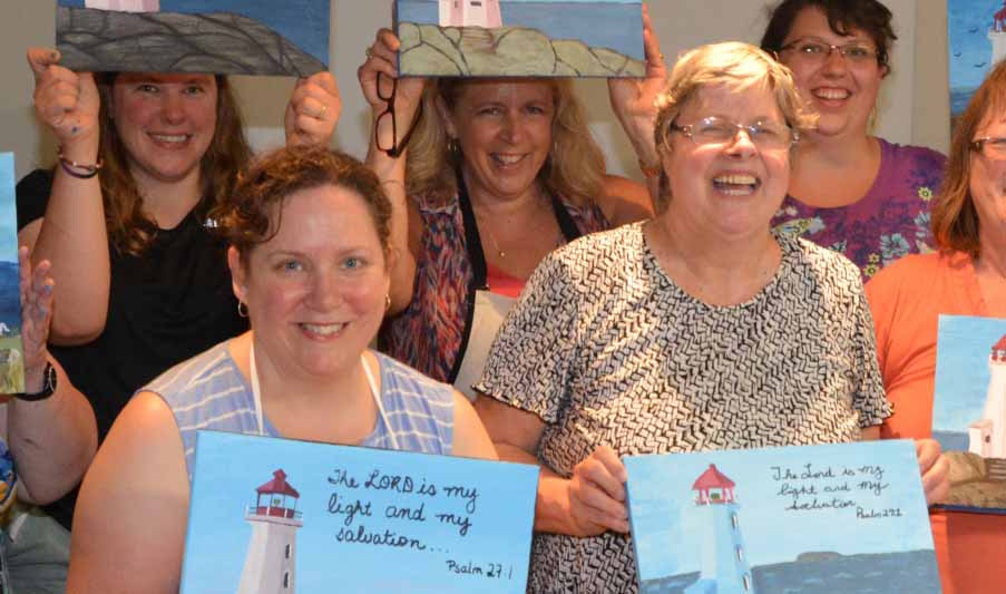 Group holding lighthouse paintings, smiling.
