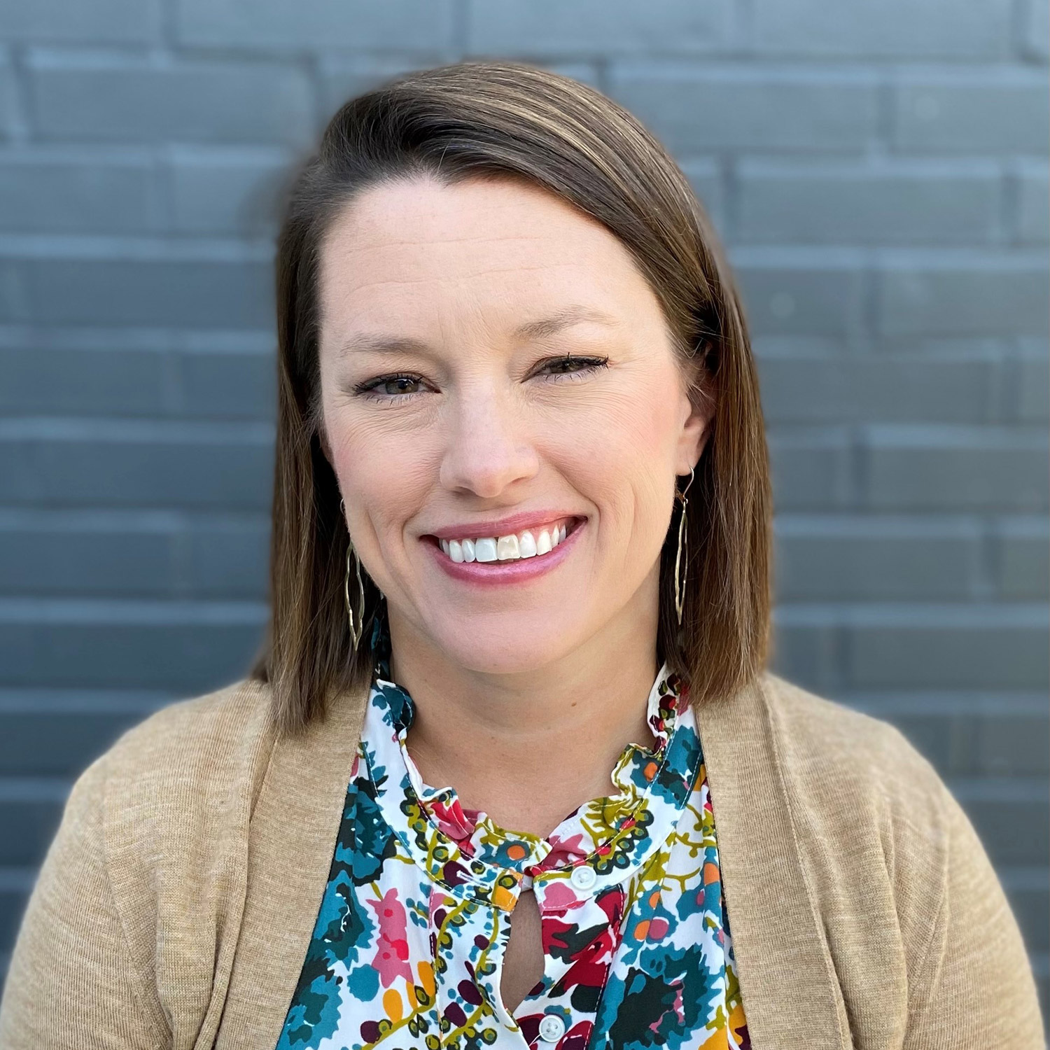 Smiling woman in colorful blouse, brick wall background.