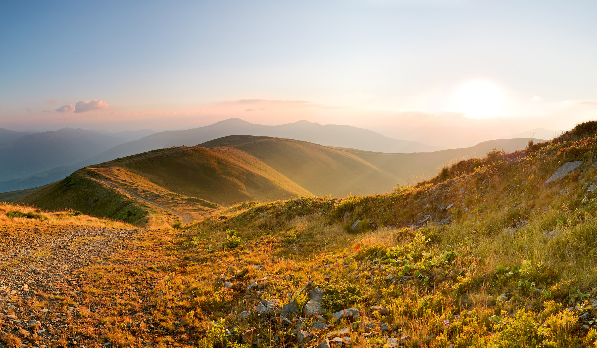 Sunset over rolling green hills and mountains.