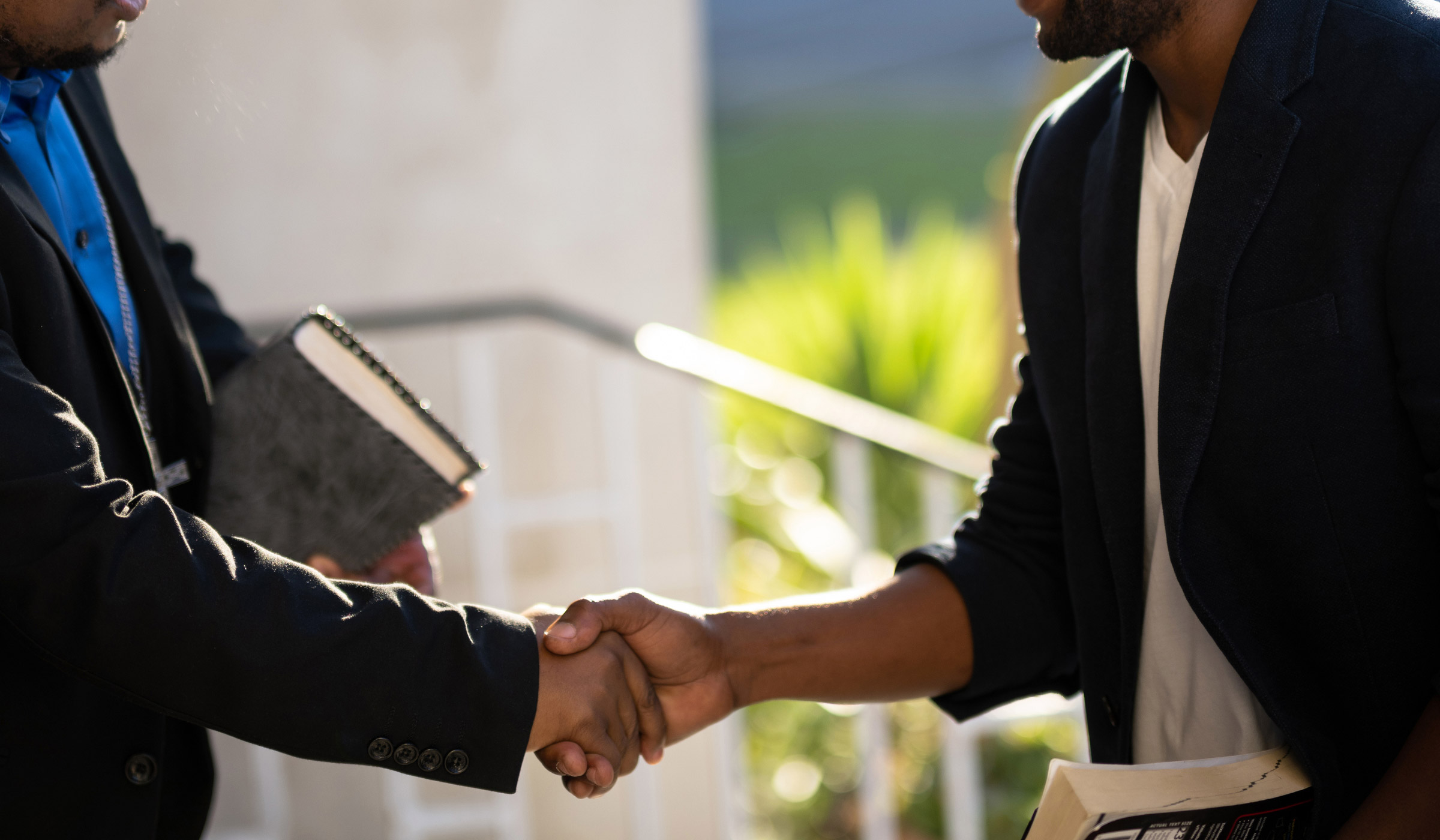 Two men shaking hands and smiling outdoors.