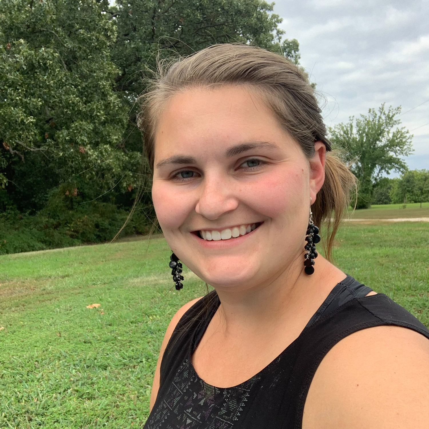 Smiling person outdoors near trees and grass