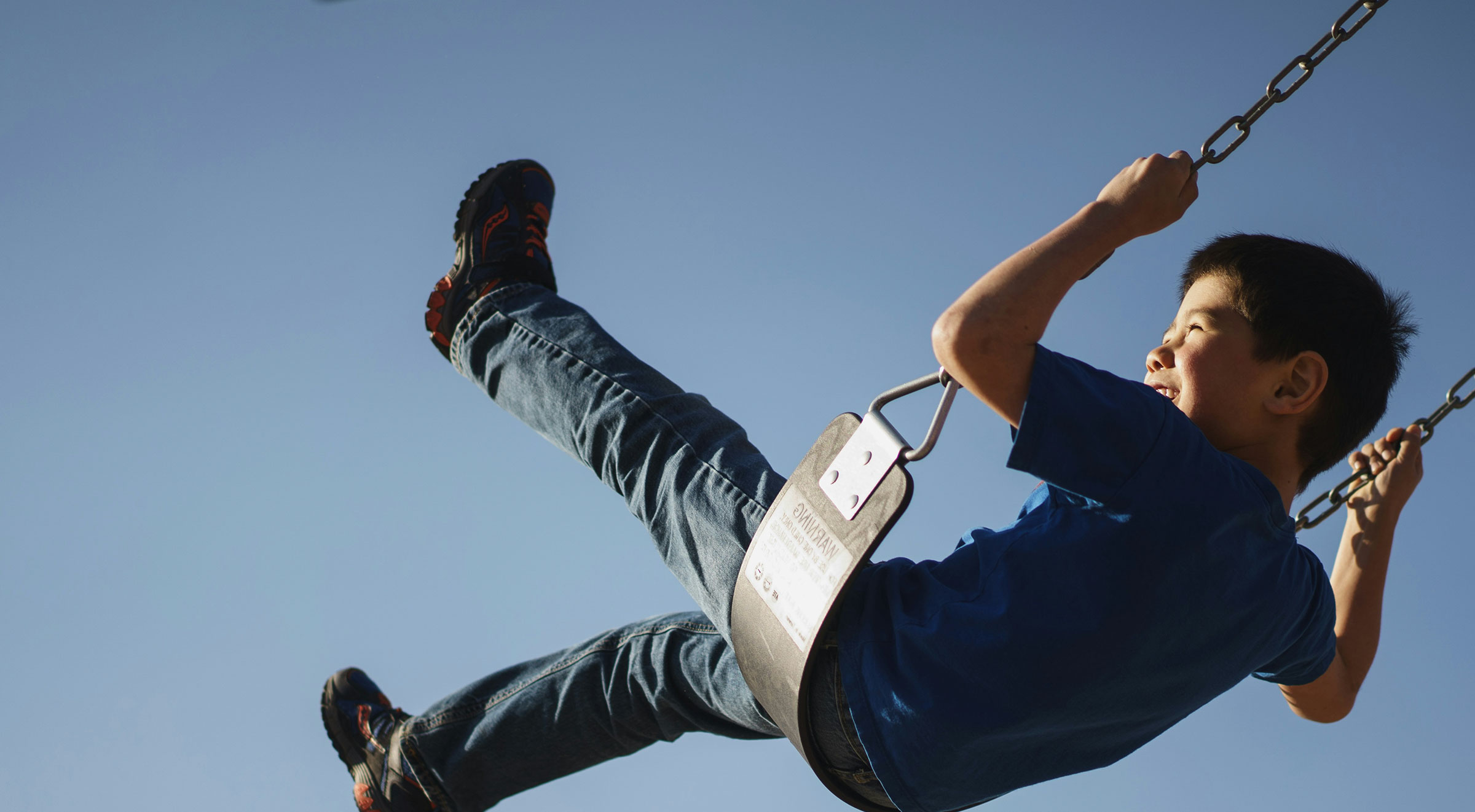 Child enjoying swinging under a clear sky.