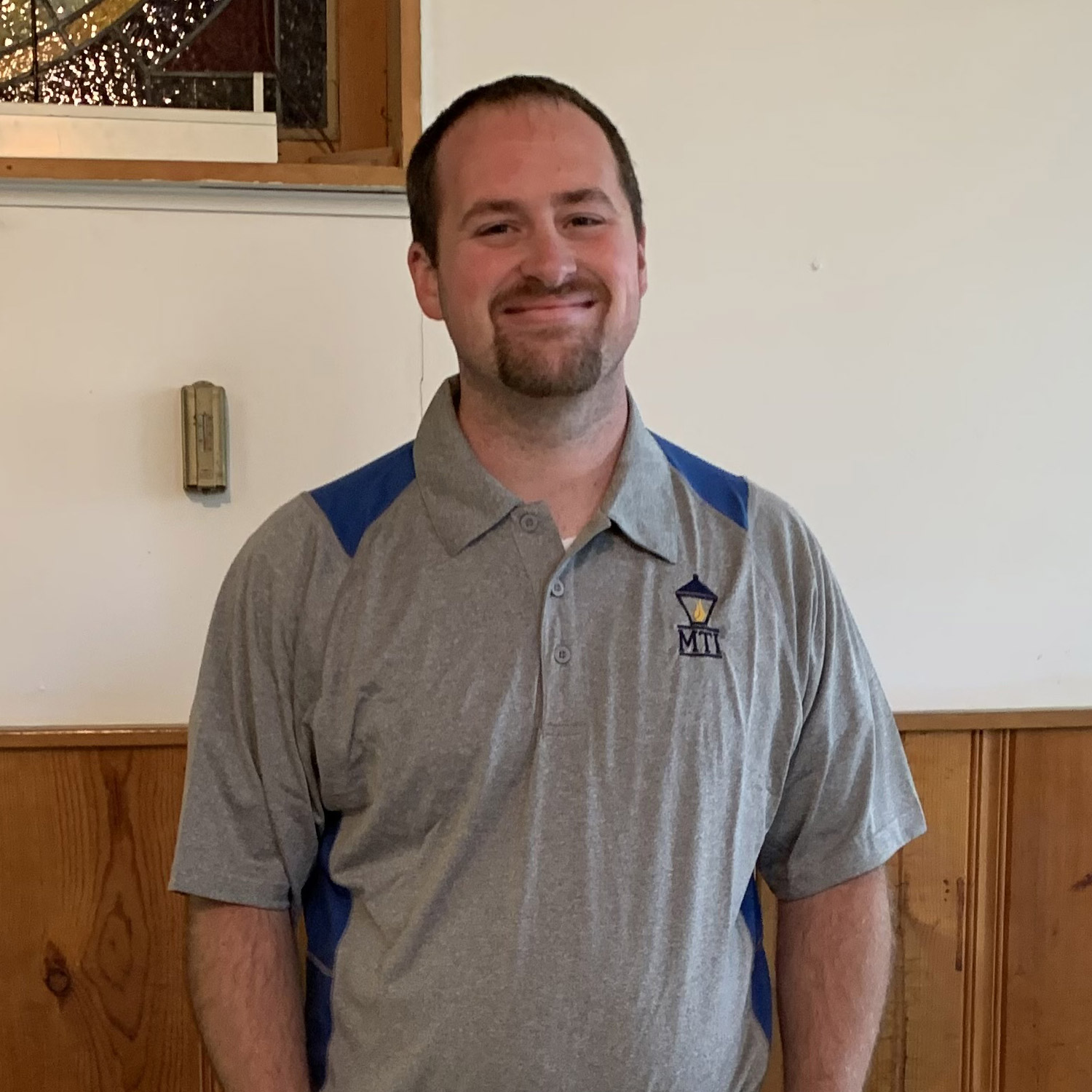 Smiling man in gray MTI shirt indoors.