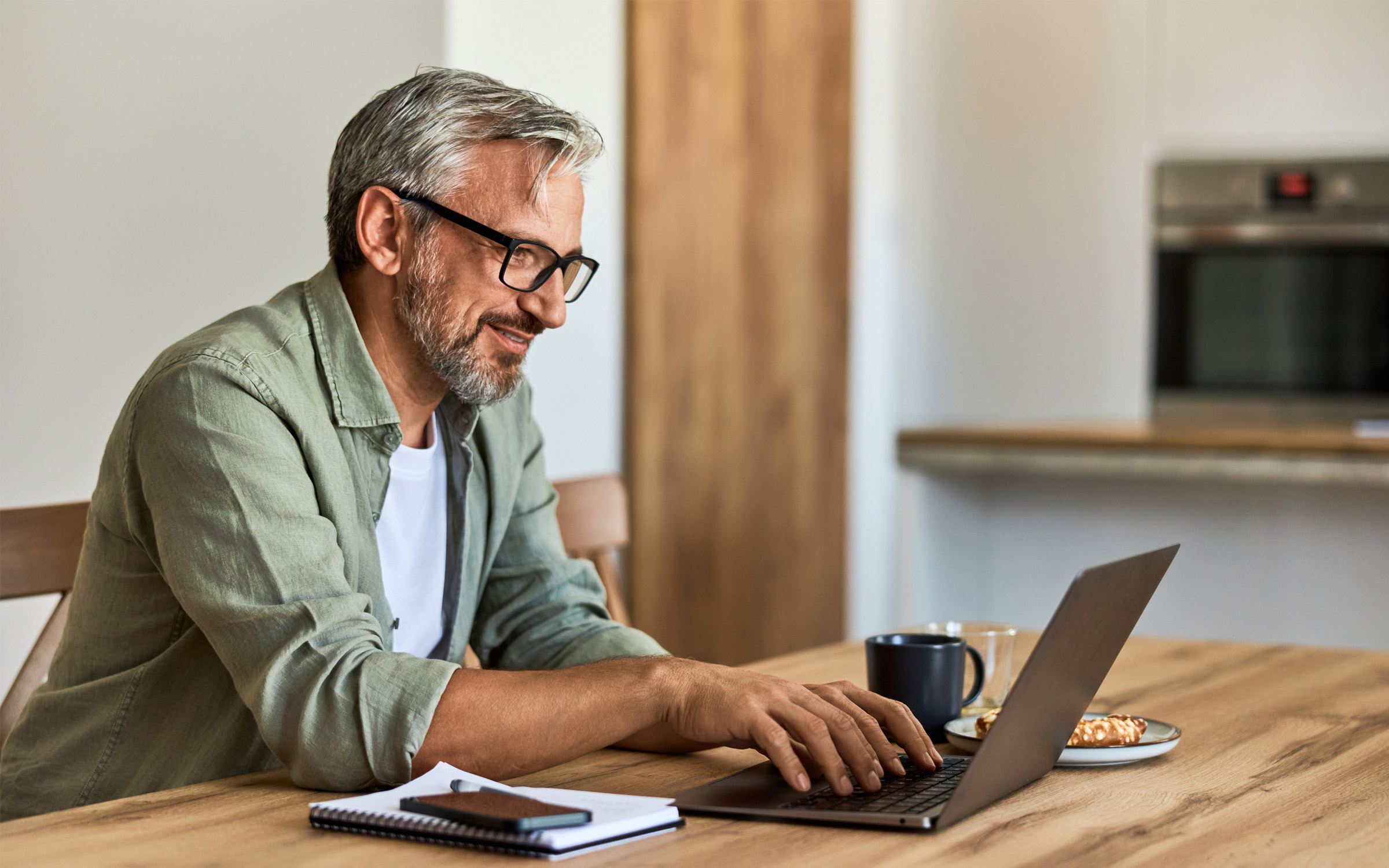 Man working on laptop at home kitchen table.