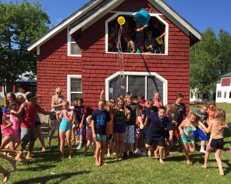 Kids playing water games outside a red house.