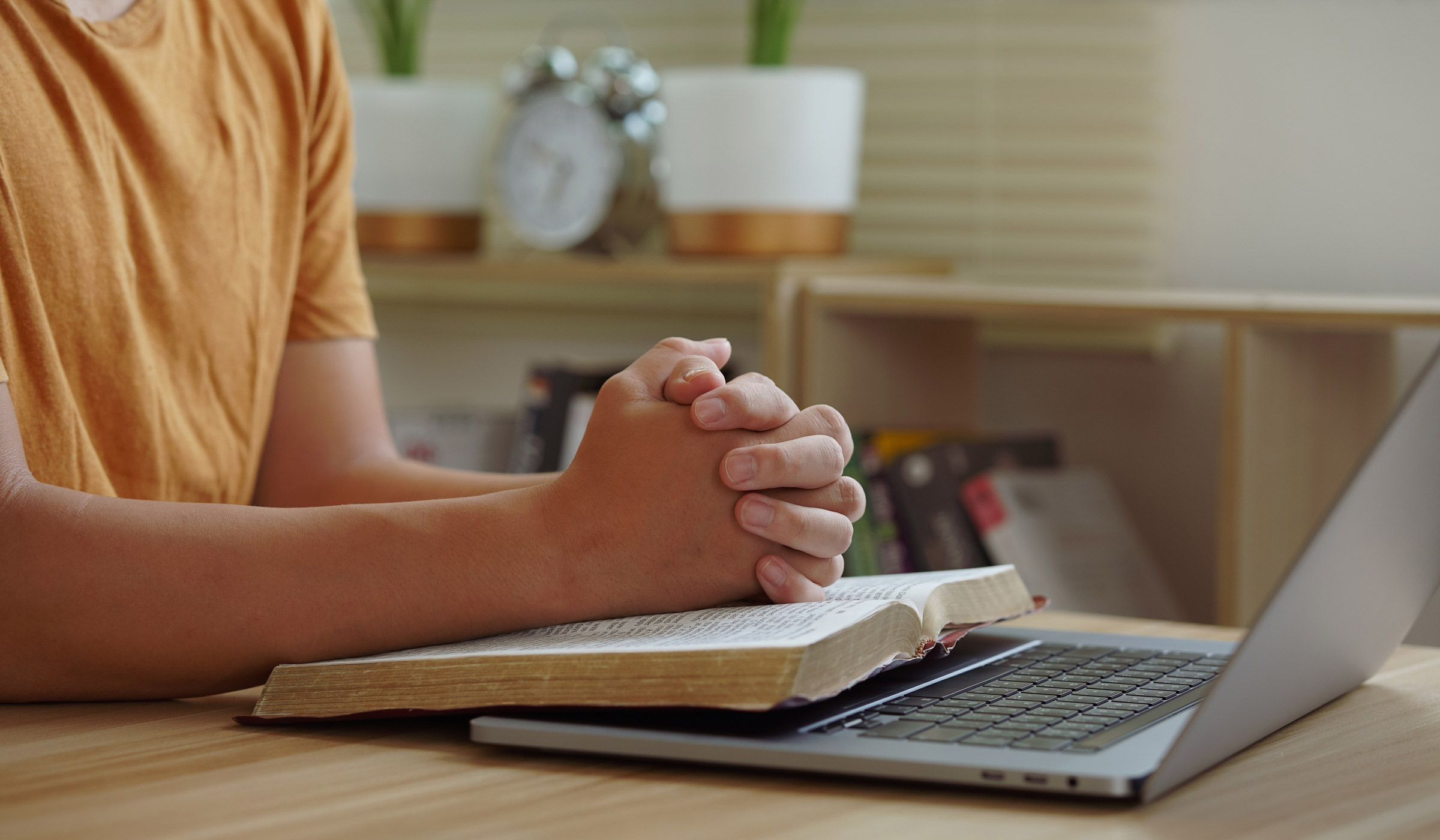 Person praying with open book and laptop