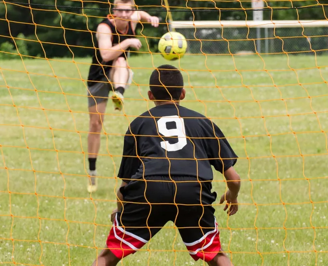 Soccer player kicks ball towards goalie.
