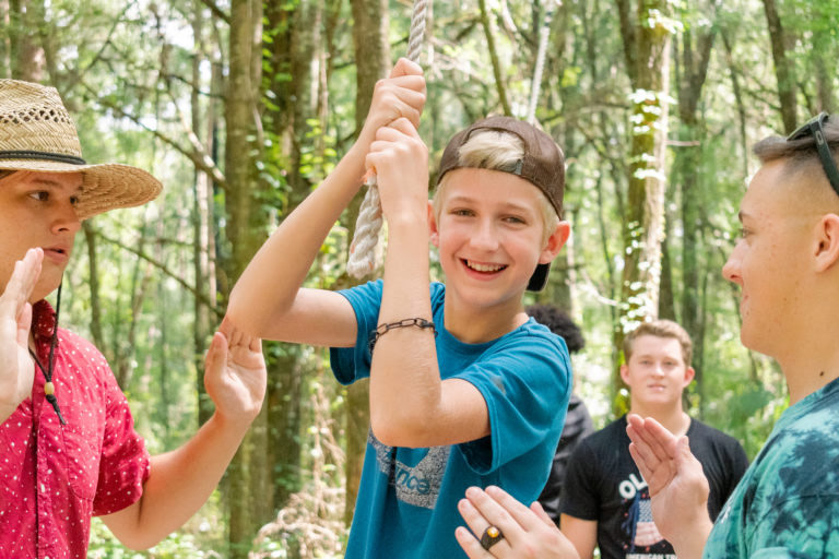 Smiling boy on rope swing in forest.