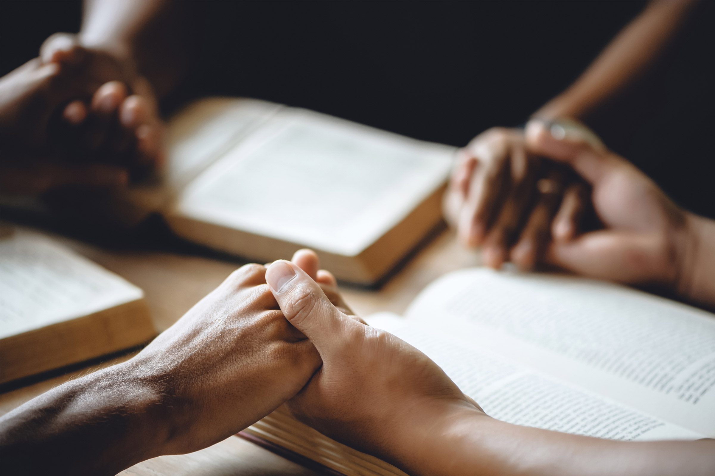 Group holding hands, praying with open books.